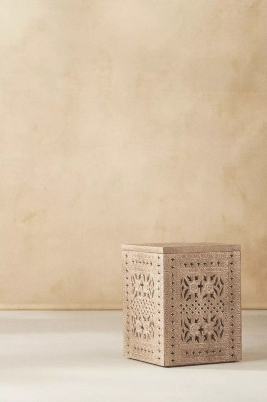 Hand-carved wood side table in natural finish, front view showing full piece on light flooring.