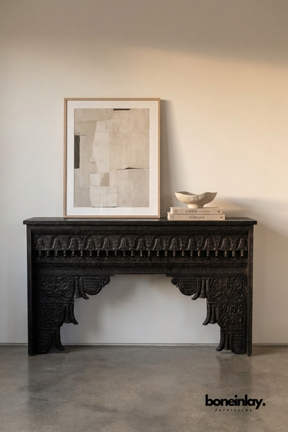 Black hand-carved console table with an ornate carved apron.
Bold scalloped corbel legs feature detailed floral relief carving.
Ebonized wood finish gives it a dramatic, statement-making look.
Styled with a framed art print and ceramic bowl on top.