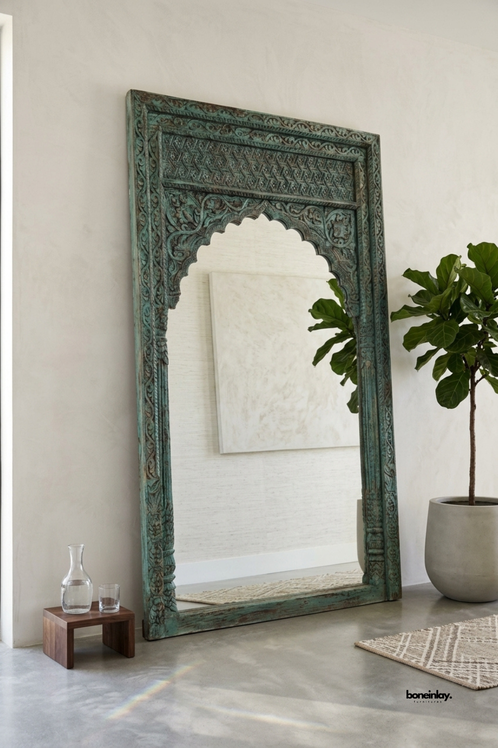 Hand-carved turquoise wooden floor mirror featuring an ornate Indian scalloped arch and detailed floral carvings. Styled leaning against a neutral plaster wall next to a potted fiddle-leaf fig tree, this vintage distressed floor-length mirror brings rustic bohemian elegance and artisan statement design to modern homes.