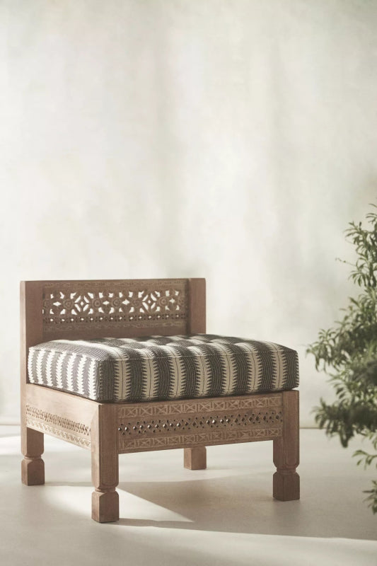Hand carved Ezana armless chair in natural wood, styled in living room with a striped cushion beside greenery.