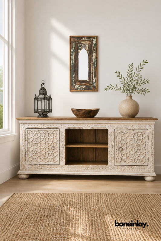 Whitewashed carved wood TV console with a star lattice door pattern.
Open center shelving sits between two intricately carved cabinet doors.
Natural wood tabletop contrasts with the whitewashed carved base.
Styled beneath a rustic arched mirror and wooden bowl.