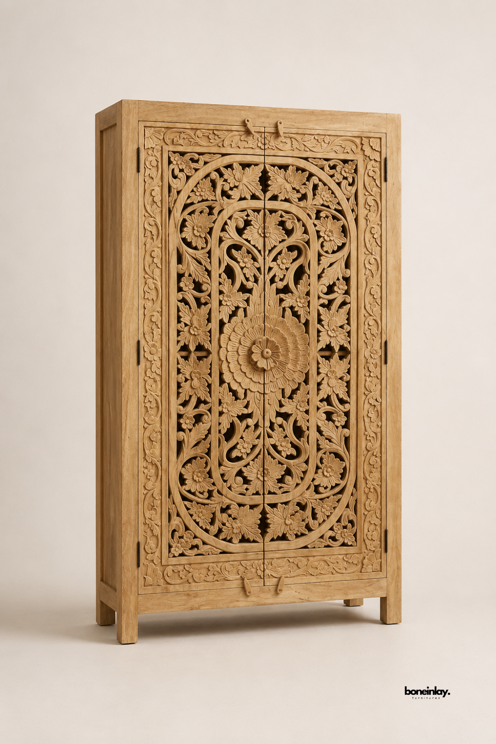 Natural mango wood wardrobe featuring a bold central floral rosette surrounded by dense scrollwork and vine carvings. Tapered wood legs and clean lines add a refined silhouette to the ornate double-door design. Photographed at an angle on a plain studio background to highlight the sculptural carved detail. A striking statement wardrobe for bedrooms and dressing rooms.