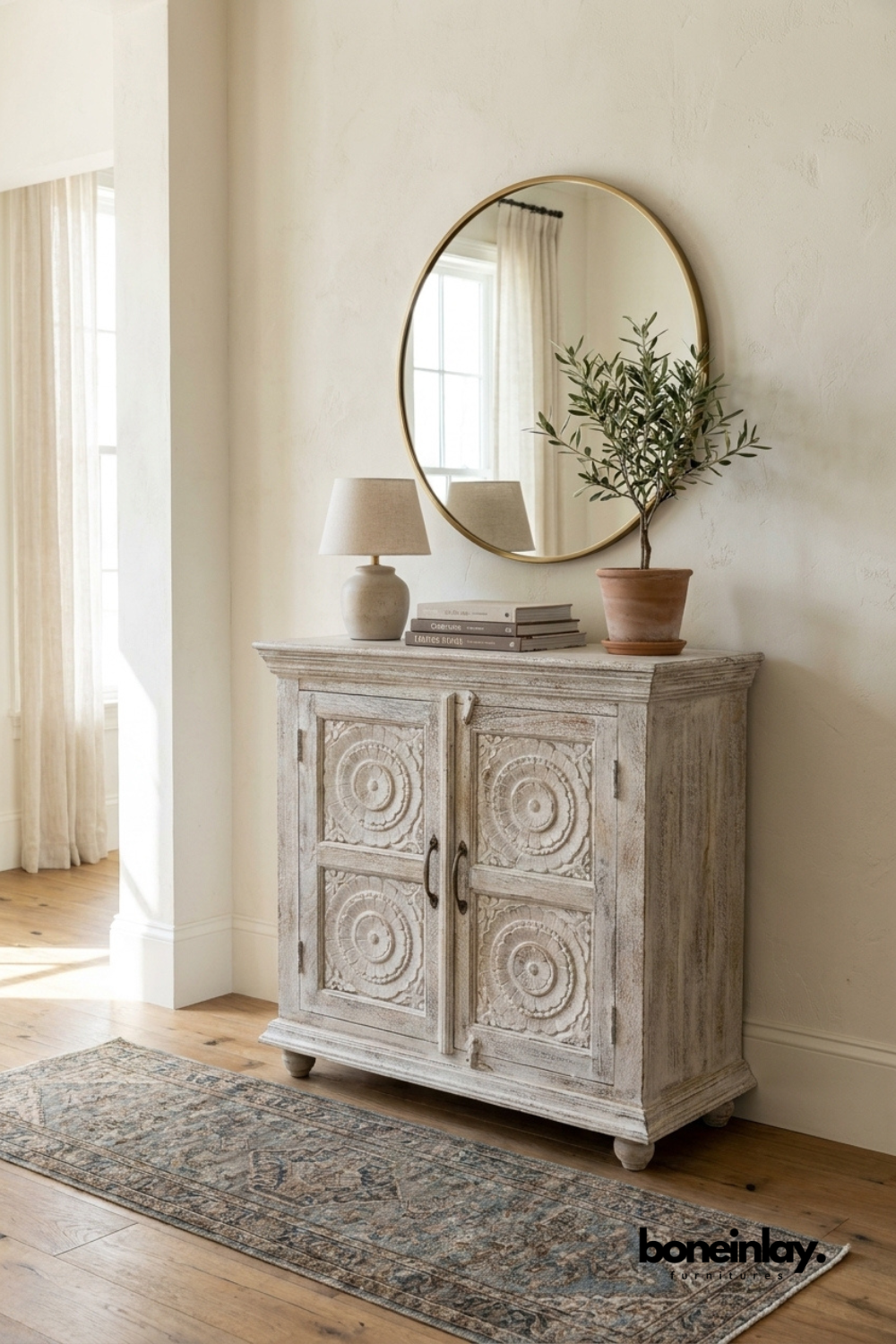 Whitewashed carved wood cabinet with round medallion door panels.
Detailed circular rosette carving repeats across all four doors.
Turned bun feet and a molded top edge add classic character.
Styled beneath a round brass mirror on a vintage-style runner rug.