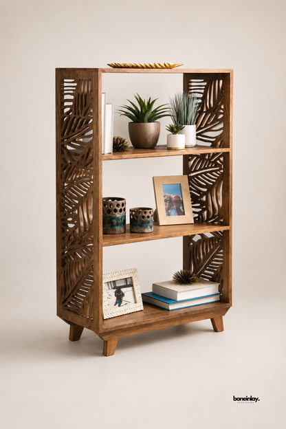 Walnut wood bookshelf featuring intricate palm leaf cutout side panels and three open display shelves. Slim tapered legs add a light, airy silhouette to the sculptural storage piece. Styled with potted succulents, ceramic vases, framed photos, and stacked books for a curated display. A striking open bookshelf for living rooms and home office styling.