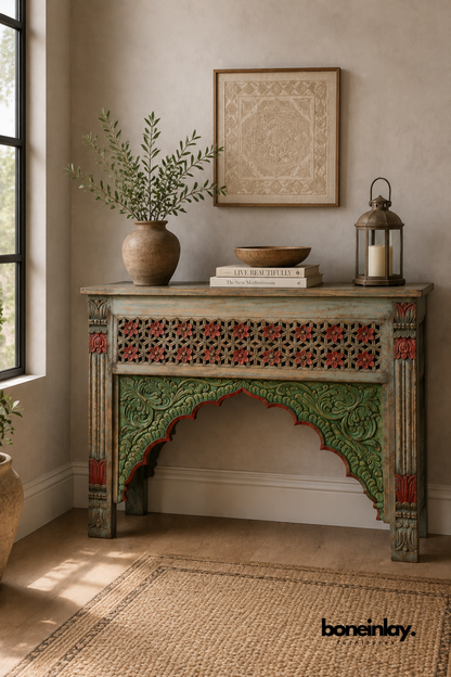 Hand-painted console table with a red, green, and blue Moorish arch design.
Carved star lattice panel and floral motifs decorate the front apron.
Fluted corner legs feature detailed red and green painted accents.
Styled with a rustic vase and lantern in a warm, bohemian entryway.