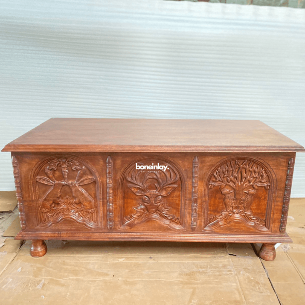 Hand carved wooden cocktail table in warm, front view showing three relief panels and short turned feet.