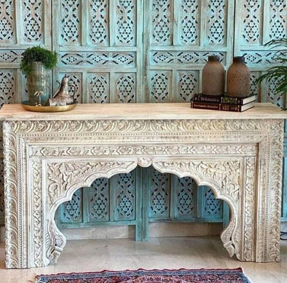 Hand carved wooden sofa table with a rustic finish, front view showing floral borders beneath plants and pottery.