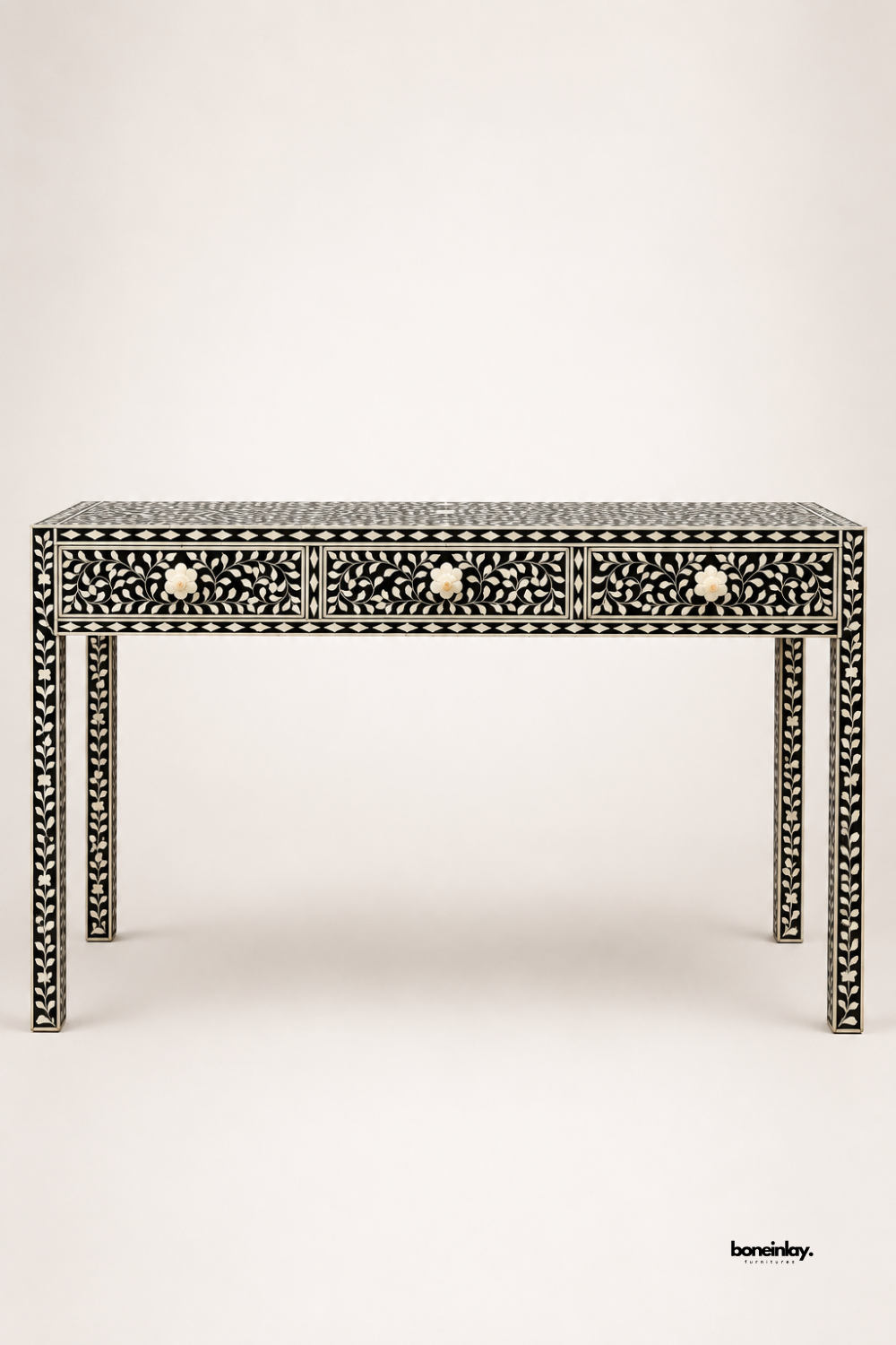 Black and white bone inlay console table featuring an intricate floral vine pattern across three drawers and all four legs. Bone flower-shaped knobs complete the elegant, fully-wrapped inlay design. Photographed on a plain studio background to showcase the detailed craftsmanship. A sophisticated statement console for entryways and hallway styling.