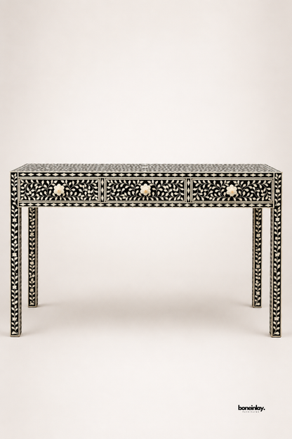 Black and white bone inlay console table featuring an intricate floral vine pattern across three drawers and all four legs. Bone flower-shaped knobs complete the elegant, fully-wrapped inlay design. Photographed on a plain studio background to showcase the detailed craftsmanship. A sophisticated statement console for entryways and hallway styling.