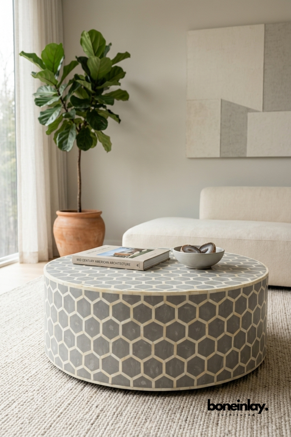 Grey and ivory bone inlay coffee table featuring a geometric honeycomb hexagon pattern around a round drum silhouette. Handcrafted inlay detailing wraps seamlessly across the top and sides. Styled with an agate bowl and coffee table book beside a terracotta planter and boucle sofa. A sophisticated round coffee table for modern living room settings.