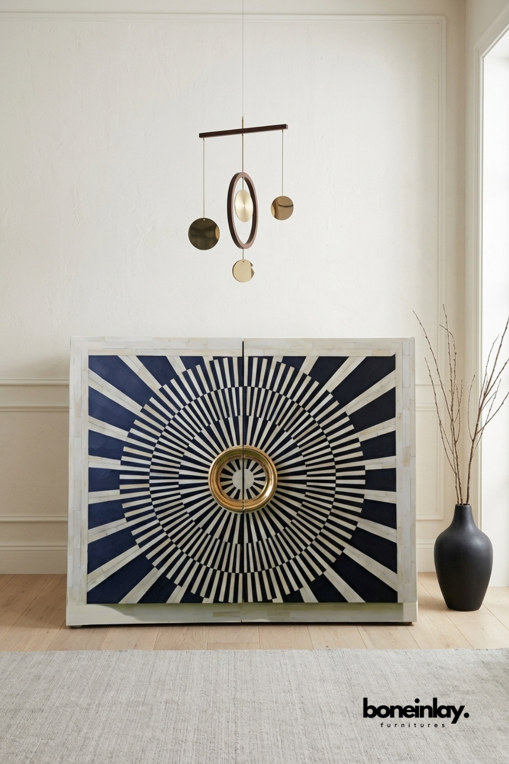 white bone inlay bar cabinet featuring a radiating sunburst pattern centered around a brass ring pull. Bold concentric striping wraps the double doors for a dramatic visual statement. Styled with a matte black vase and a hanging brass kinetic mobile sculpture overhead. A striking bar cabinet or accent piece for eclectic and maximalist interiors.