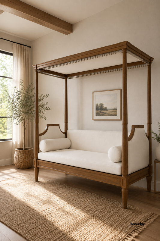 Handmade wooden canopy daybed styled in a sunlit living room featuring natural wood beams, sheer curtains, and an olive tree aesthetic. This luxury four-poster lounge daybed with delicate tassel trim and soft white upholstery brings sophisticated artisan charm to modern homes.