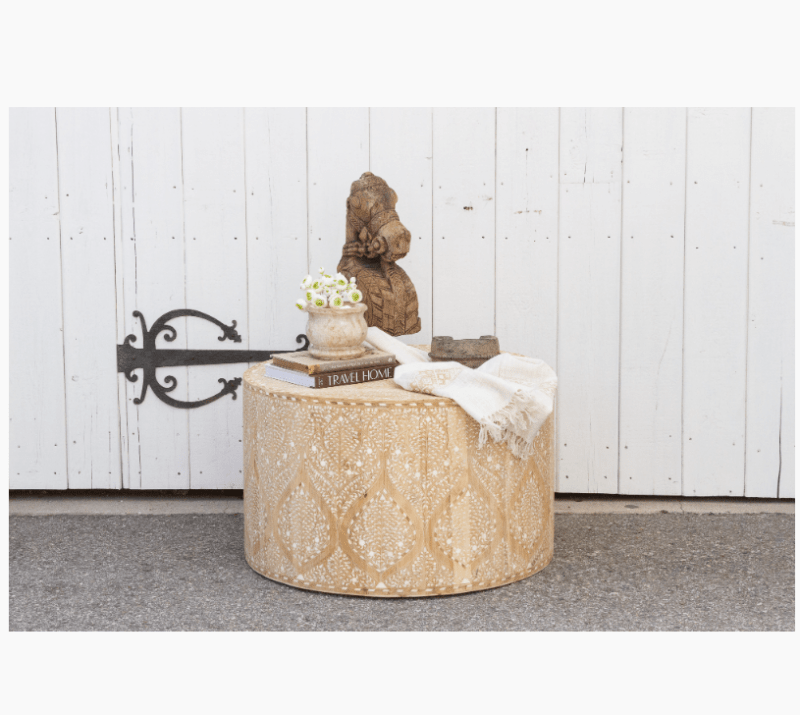 Styled bone inlay drum coffee table with books and flowers on top, white fence background, bohemian artisan decor, handcrafted natural wood furniture