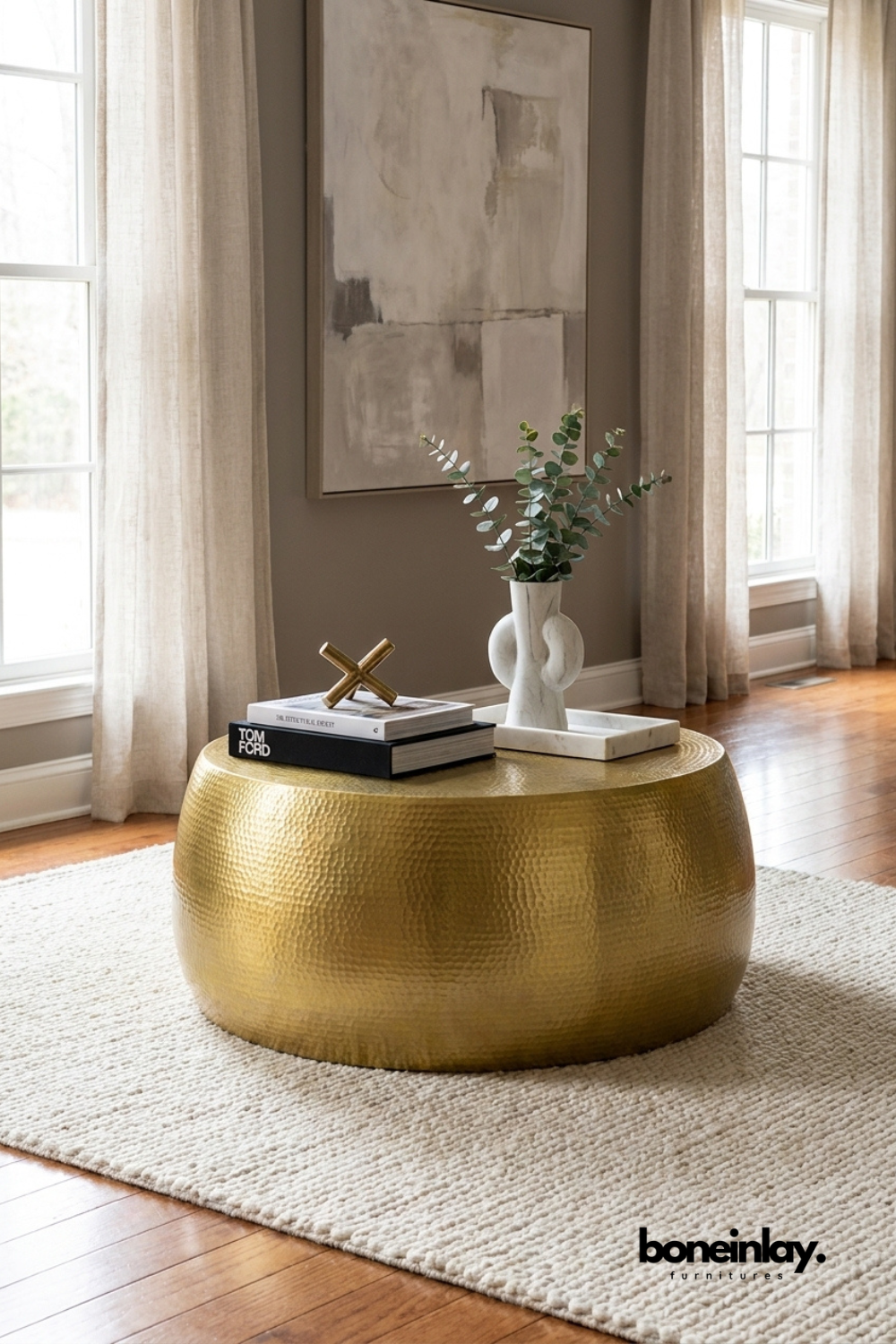 Hammered brass round coffee table with textured metal finish and drum silhouette styled with decorative accessories