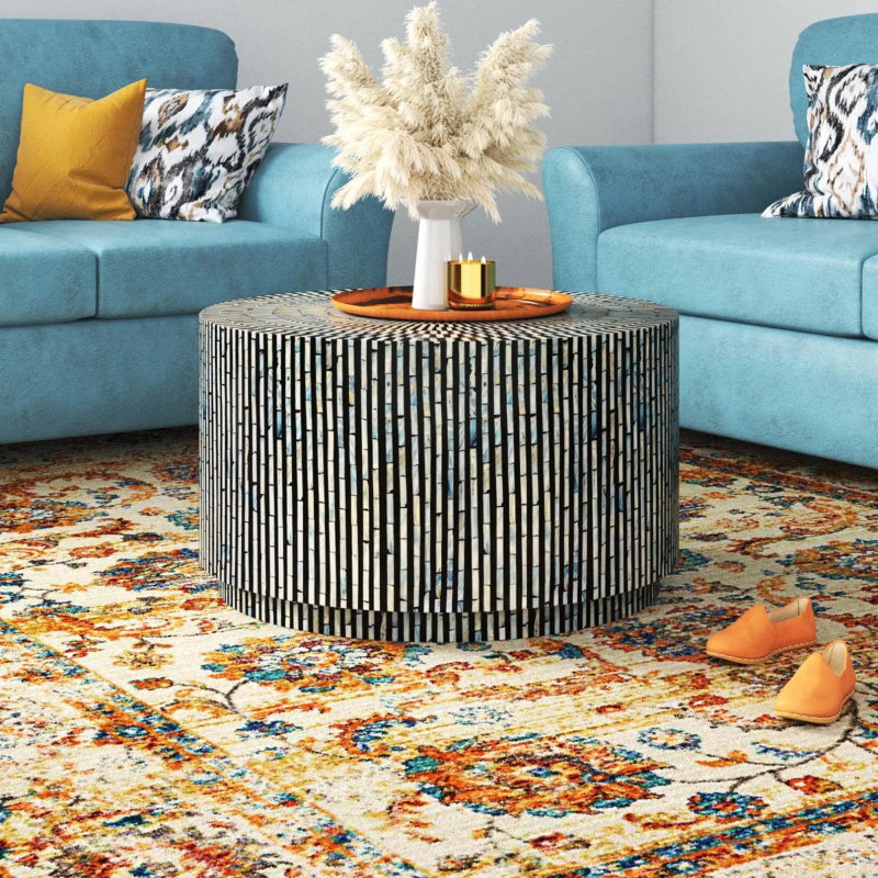 Handcrafted black and white bone inlay drum coffee table styled in a blue sofa living room with pampas grass decor on top, artisan round striped inlay furniture in real home setting