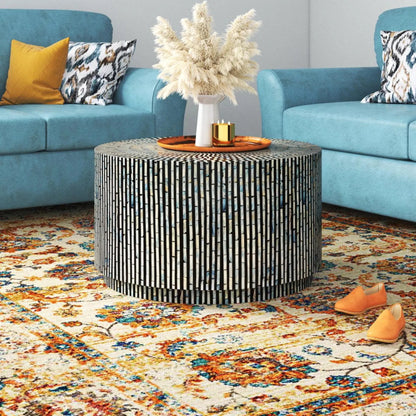 Handcrafted black and white bone inlay drum coffee table styled in a blue sofa living room with pampas grass decor on top, artisan round striped inlay furniture in real home setting