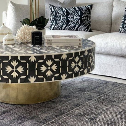 Handcrafted bone inlay mosaic coffee table with intricate black and white floral pattern and gold metal base, placed in a cozy living room styled with a grey sofa and decorative cushions