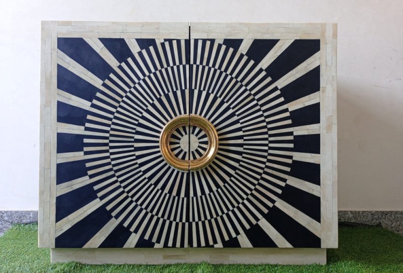 Handcrafted bone inlay bar cabinet with black-and-white radial decoration across its double doors. The patterned front is paired with prominent circular gold-finished handles, creating a high-contrast geometric appearance. Made with solid wood, black resin, and ivory bone inlay, the cabinet offers decorative storage for spirits, glassware, or media essentials.