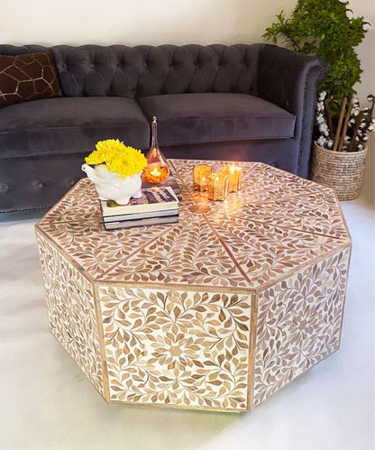 Handcrafted octagonal resin coffee table with leaf bone inlay pattern in champagne and beige, placed in a dark sofa living room setting with yellow flowers and lit candles
