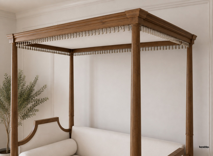 Handmade wooden canopy daybed featuring rich natural grain posts, delicate hanging tassel fringe trim, and plush off-white upholstery. This artisan-crafted statement daybed brings sophisticated lounging and timeless elegance to luxury UK living spaces.
