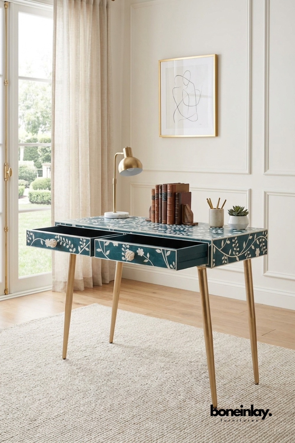 Teal bone inlay writing desk with a hand-inlaid floral vine pattern.
Two drawers feature carved bone flower pulls for a decorative touch.
Slim tapered brass legs give it a light, modern stance.
Styled with a brass desk lamp and stacked leather-bound books.