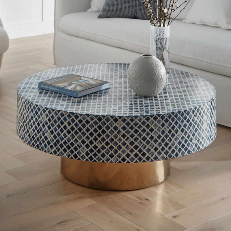 Handmade blue and white lattice bone inlay round coffee table with brass drum base, styled with book and ceramic vase in living room