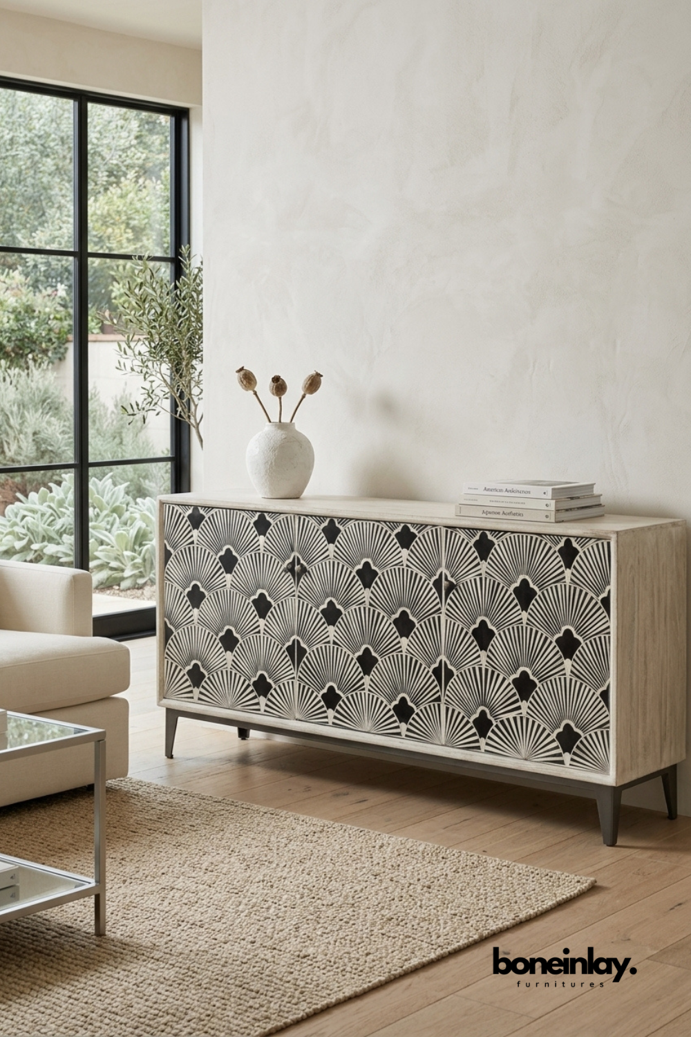 Natural wood media unit featuring a black and ivory scalloped fan bone inlay pattern across three doors. Finished with tapered dark wood legs for a warm mid-century inspired look. Styled with a ceramic vase, dried botanicals, and stacked books near a glass coffee table. An eye-catching storage piece for living and dining room settings.