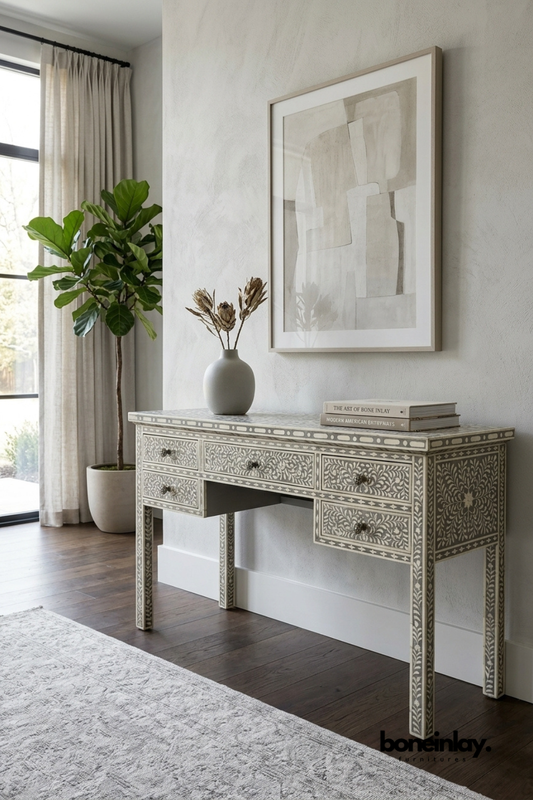 Grey and ivory bone inlay console desk featuring an intricate floral vine pattern across five drawers. Tapered legs with matching inlay detail create a slim, elegant silhouette for functional use. Styled with a ceramic vase, dried botanicals, and stacked books beneath framed abstract art. A refined writing desk or entryway console for bohemian and transitional interiors.Handmade Bone Inlay Console Table | Custom Made Make Up Vanity Table with Drawers