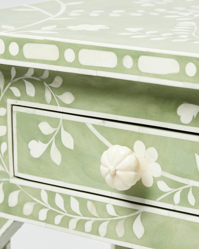 Detailed view of the drawer front on a sage green bone inlay console table featuring a hand-carved white bone flower knob and trailing vine and leaf inlay pattern