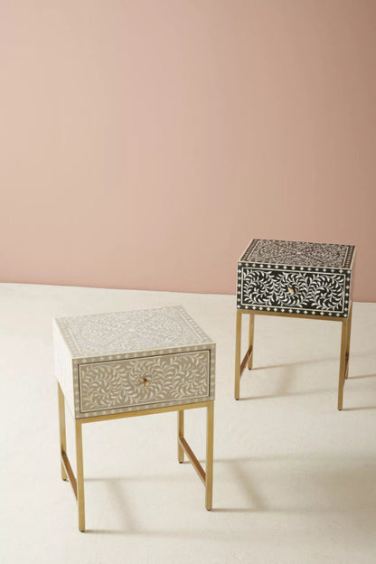 Pair of handmade bone inlay floral design nightstands in grey and dark colour options, featuring all-over vine leaf pattern and slim brass metal legs on a pink backdrop.