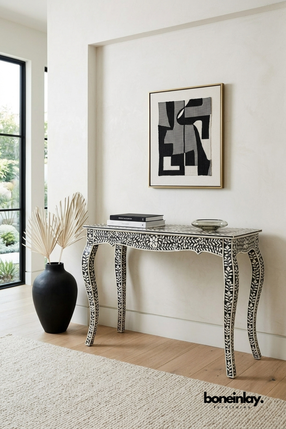 Black and white bone inlay console table featuring an intricate floral vine pattern across the apron and curved cabriole legs. Scalloped skirt detailing adds a graceful, vintage-inspired silhouette. Styled with a black ceramic vase, stacked books, and a smoked glass bowl beneath framed abstract art. An elegant statement console for entryways and hallway styling.