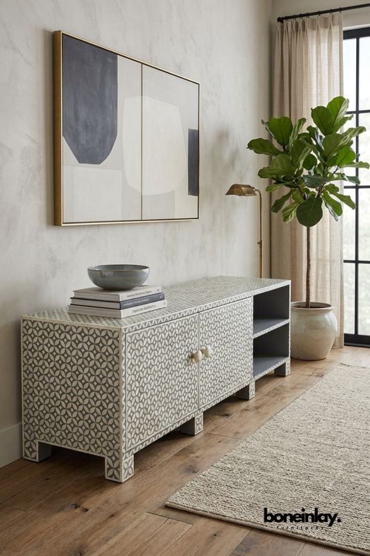 Grey and ivory bone inlay TV console featuring a geometric floral pattern with two cabinet doors and open shelving. Styled with a ceramic bowl, design books, brass floor lamp, and a fiddle leaf fig plant. Combines closed storage and display shelving for functional versatility. A stylish media console for modern and transitional living rooms.