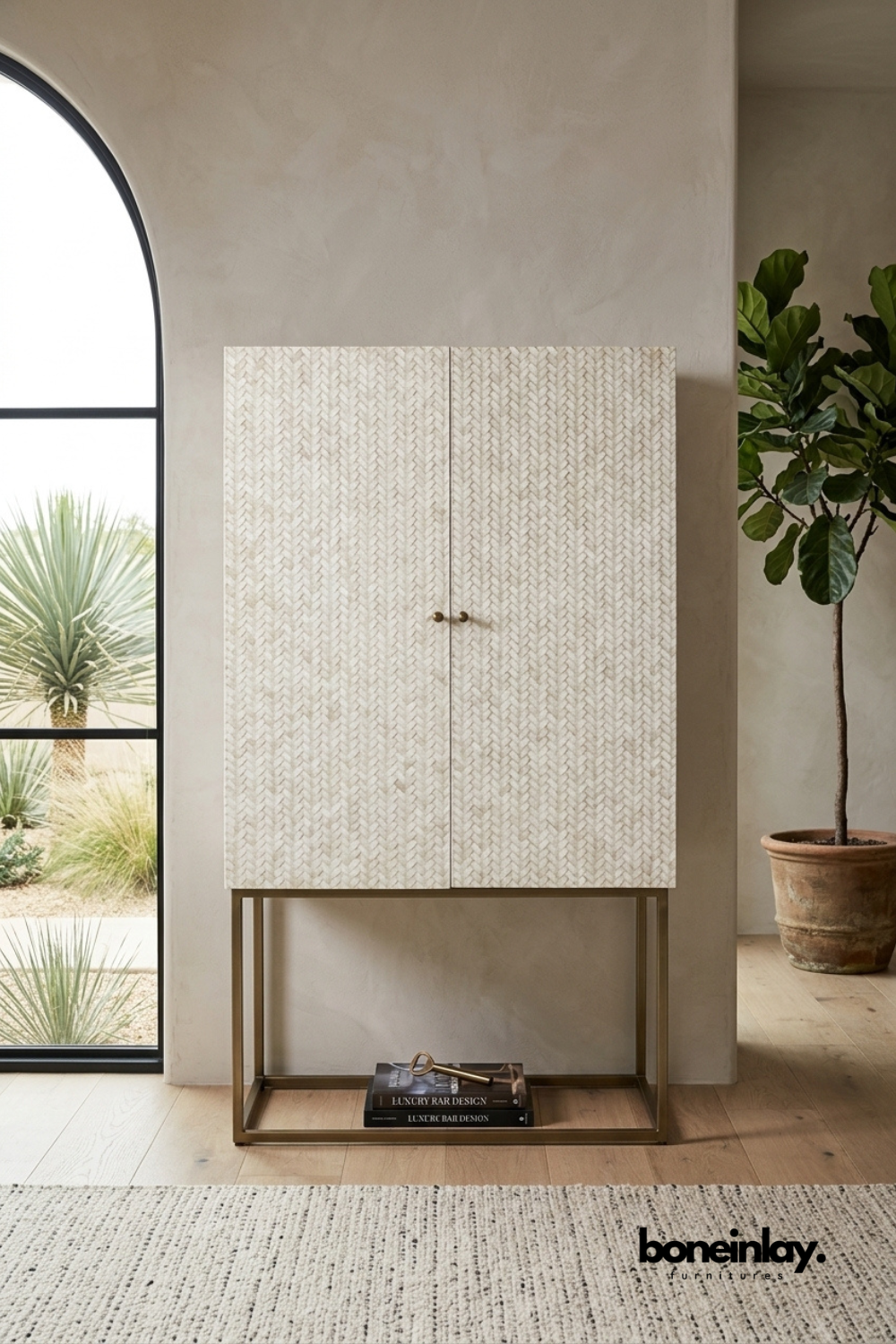 Ivory bone inlay cabinet featuring a woven braid-textured pattern on double doors with brass knob hardware. Elevated on a slim brass metal stand for an airy, elegant silhouette. Styled beside a potted fiddle leaf fig near an arched doorway with desert landscaping. A striking storage cabinet that blends organic texture with modern metal accents.
