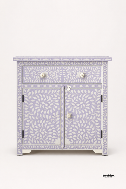 Handmade bone inlay storage cabinet in lavender with white leaf vine inlay, one drawer and two-door cupboard with bone flower knobs, photographed on a clean white background.