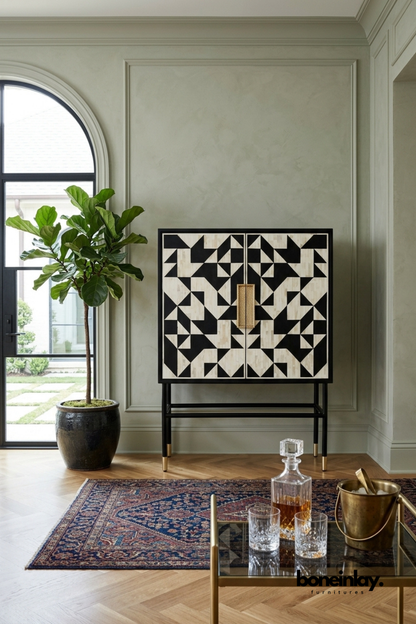 Black and white geometric bone inlay bar cabinet featuring a bold triangular mosaic pattern on double doors. Elevated on a slim black metal stand with brass-capped feet and a woven rattan door pull. Styled with crystal decanters and a brass ice bucket on a vintage Persian rug. A sophisticated bar cabinet for elegant entertaining spaces and living rooms.