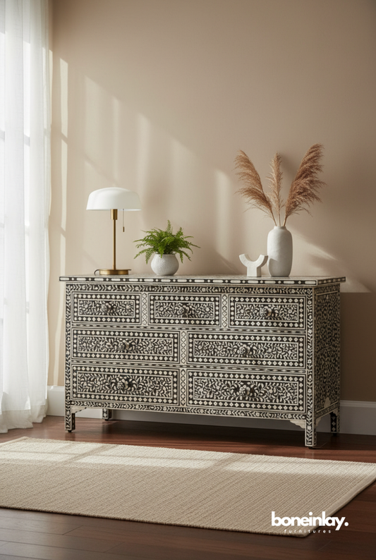 A luxury floral bone inlay seven-drawer dresser in a high-contrast black and white monochrome finish. The piece features intricate vine and blossom motifs hand-laid into a matte black resin, accented with hand-carved floral knobs and a matching inlaid border. Shown in a bright, modern interior, this artisanal chest of drawers blends traditional Indian craftsmanship with a sophisticated bohemian aesthetic.