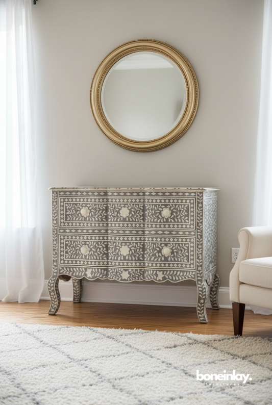 Grey floral bone inlay 2-drawer French dresser with curved cabriole legs and ivory flower knobs, styled in a bright living room with a round gold mirror – handcrafted luxury furniture by Bone Inlay Furnitures.