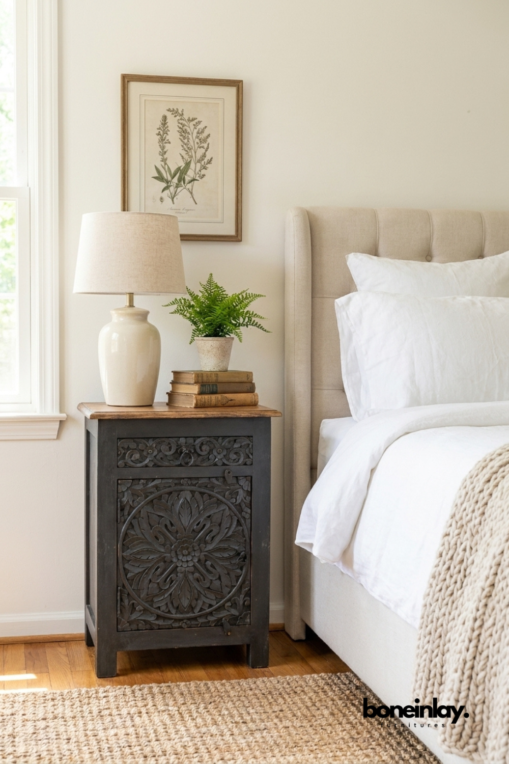 Handcrafted black carved solid wood bedside cabinet with intricate floral medallion door, natural wood top, single door storage, and traditional hand-carved detailing, styled beside an upholstered bed in a modern farmhouse bedroom.