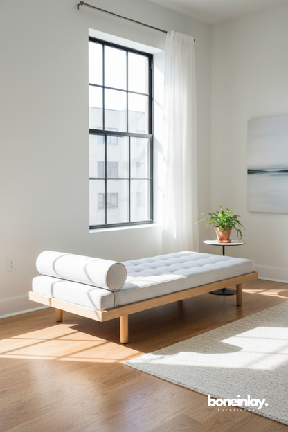 Minimalist upholstered daybed with bolster cushion in a bright sunlit interior.