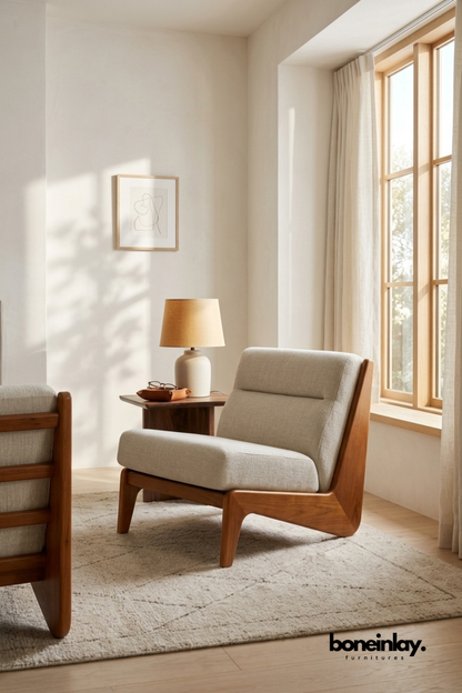 Mid-century teak wood frame accent chair with angular legs.
Upholstered in grey woven fabric with a padded lumbar cushion.
Solid wood frame wraps around the seat for a sculptural look.
Placed by a sunlit window beside a walnut side table.