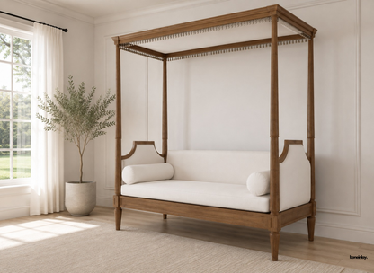 Artisan-crafted solid wooden canopy daybed styled in a bright British living room with soft neutral drapery, matching bolster pillows, and a textured area rug. This luxury four-poster daybed combines organic warmth with refined comfort for modern UK home interiors.