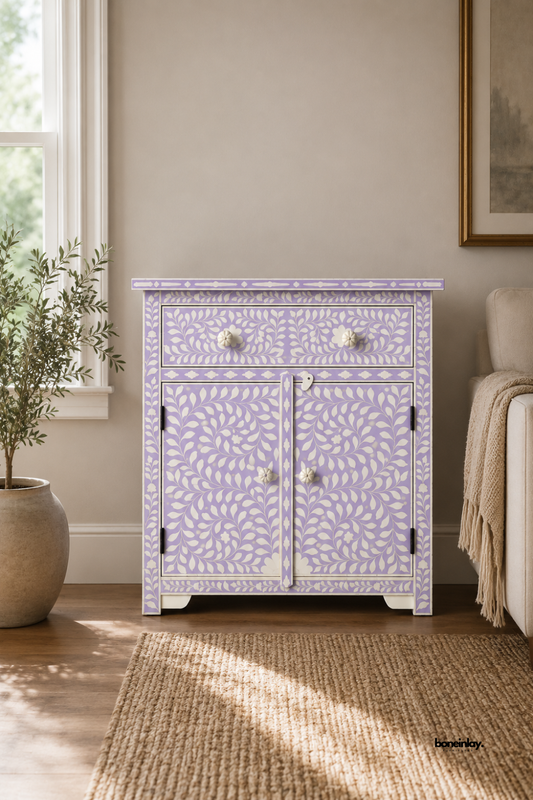 Handmade bone inlay lavender cabinet with white floral vine pattern, one drawer and double-door cupboard, bone knobs, styled in a warm living room with a jute rug and potted olive tree.