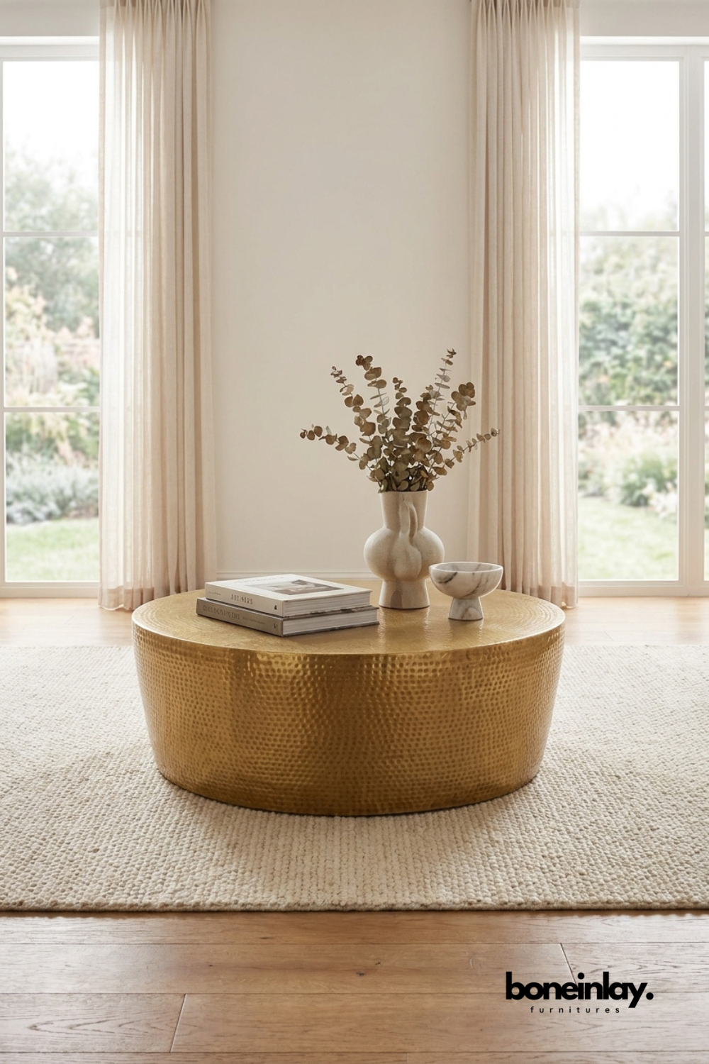 Round hammered brass coffee table with textured metal finish and drum silhouette styled in a neutral contemporary living room