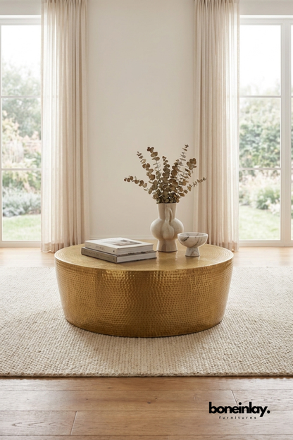 Round hammered brass coffee table with textured metal finish and drum silhouette styled in a neutral contemporary living room