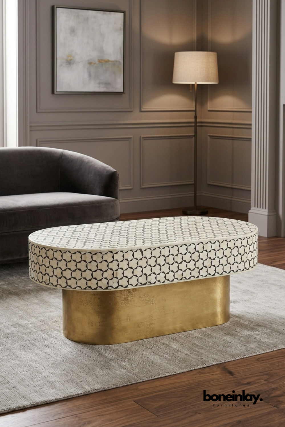 Oval bone inlay coffee table featuring an intricate black and white mosaic star pattern across the tabletop. Elevated on a solid brass drum-style pedestal base for a striking contrast of texture and shine. Styled in a refined wood-paneled living room beside a velvet sofa and floor lamp. A luxurious statement coffee table for formal and eclectic interiors.