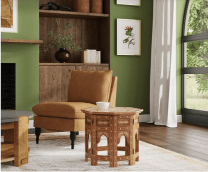 Wide interior view of Hexagonal Bone Inlay Teak Wood Bohemian Side Table in a green living room with wooden shelving and caramel chair, showcasing the table as a statement handcrafted Indian accent furniture piece.