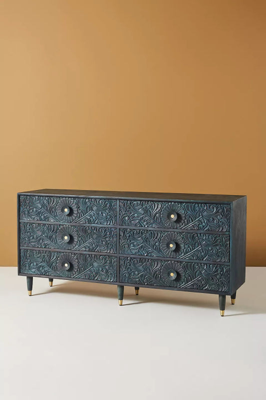Angled full view of the indigo Gulliver six-drawer bureau against a plain background, showing its carved front.