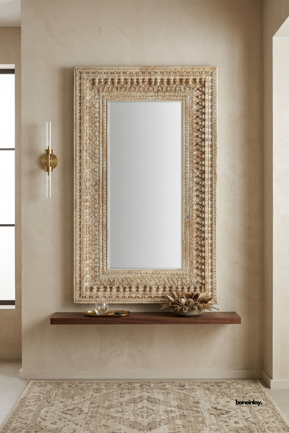 Hand-carved whitewashed wooden wall mirror featuring a multi-tiered carved border with traditional bead and floral relief work. Mounted above a minimalist floating walnut ledge in a warm neutral entryway, this vintage artisan accent mirror brings rustic elegance and timeless craftsmanship to luxury home interiors.