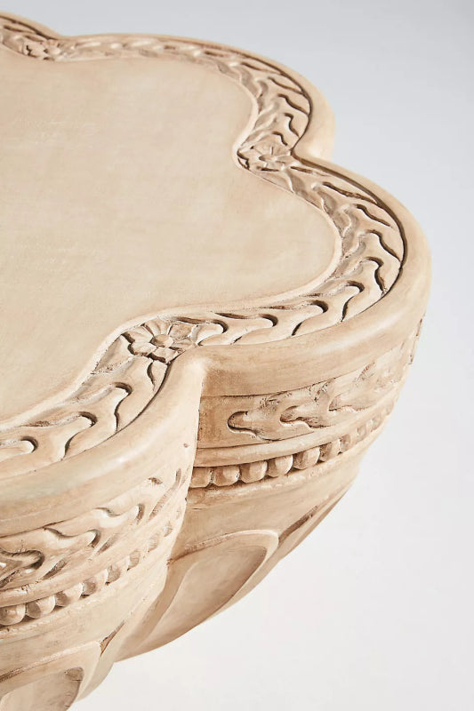 Round center table in warm light-washed wood, a lotus-inspired handmade piece with carved scalloped edges on display