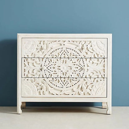Front view of a hand-carved whitewashed three-drawer wood dresser with an intricate central mandala carving and matching wood knobs.